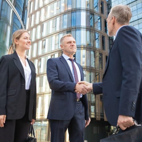 Confident business partners meeting in city, shaking hands near office building. Low angle shot. Cooperation and partnership concept